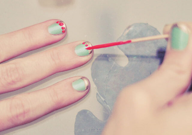 Red dots being painted onto mint-green fingernails with a toothpick.
