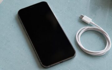 A smartphone and a white charging cable on a pale blue counter.