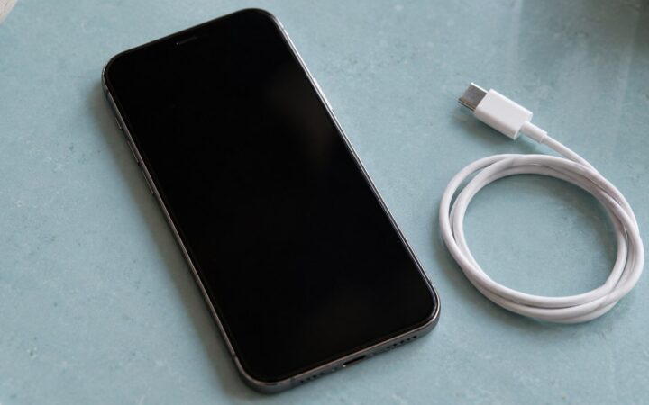 A smartphone and a white charging cable on a pale blue counter.