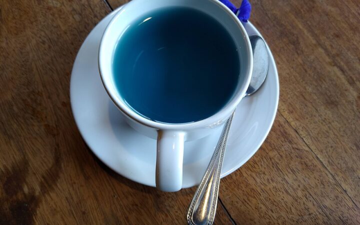 A cup of blue butterfly-pea flower tea on a wooden table.
