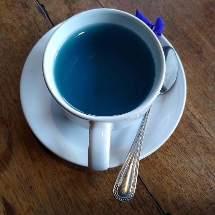 A cup of blue butterfly-pea flower tea on a wooden table.