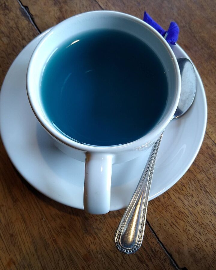 A cup of blue butterfly-pea flower tea on a wooden table.