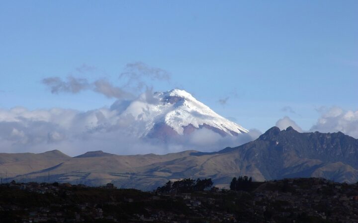 A snow-covered Andean volcano rises beyond green hills near Quito, Ecuador.