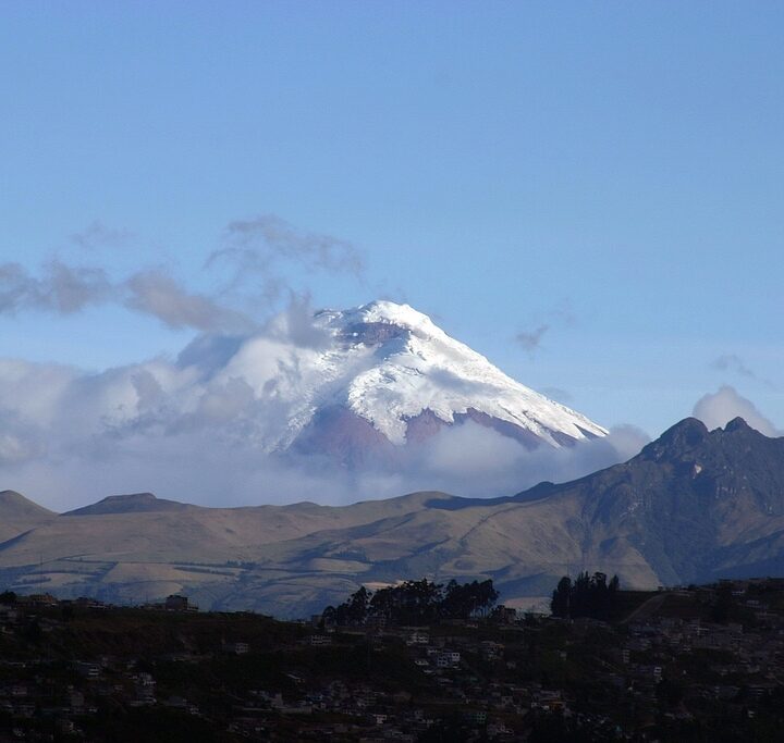 A snow-covered Andean volcano rises beyond green hills near Quito, Ecuador.