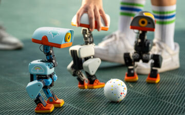 Three Microduck robots gathered around a ball on a games surface