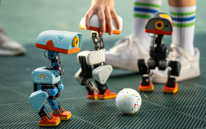 Three Microduck robots gathered around a ball on a games surface