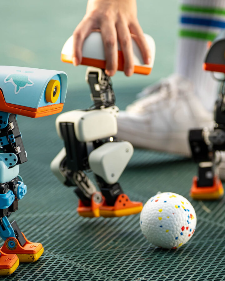 Three Microduck robots gathered around a ball on a games surface