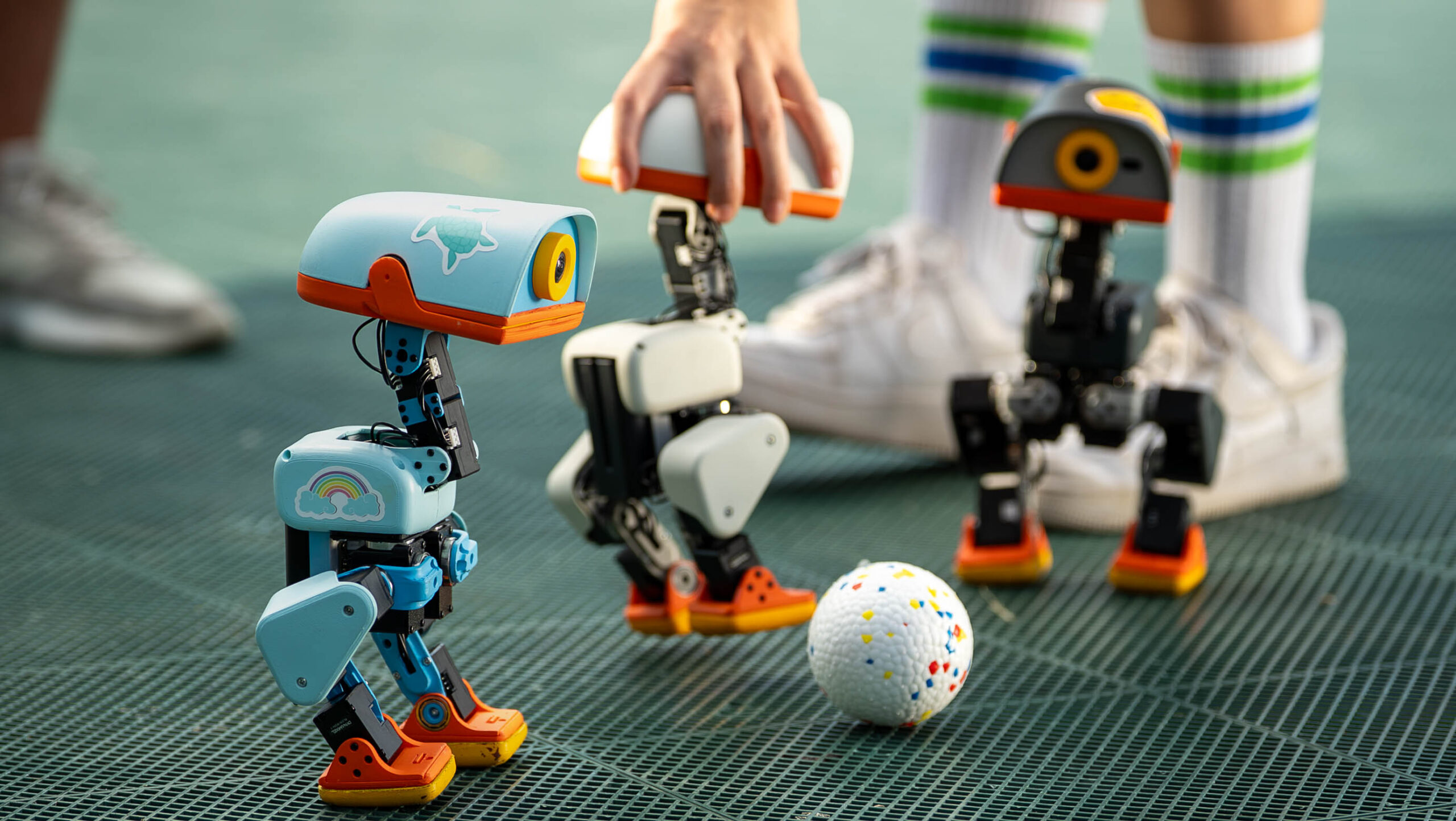 Three Microduck robots gathered around a ball on a games surface