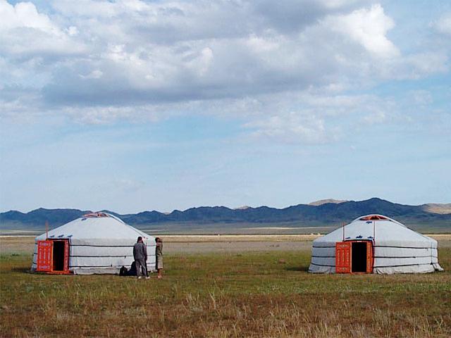 Two traditional white gers on an open grassy Mongolian steppe.